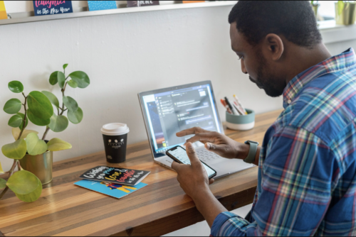 Man looking at phone with laptop in the background